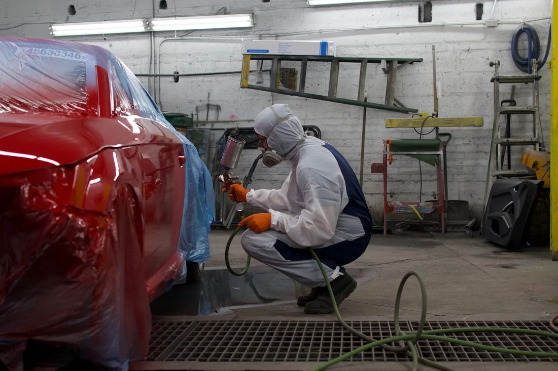 Painter in full spray gear refinishing a red car at C & A Auto Body Shop in Chicago